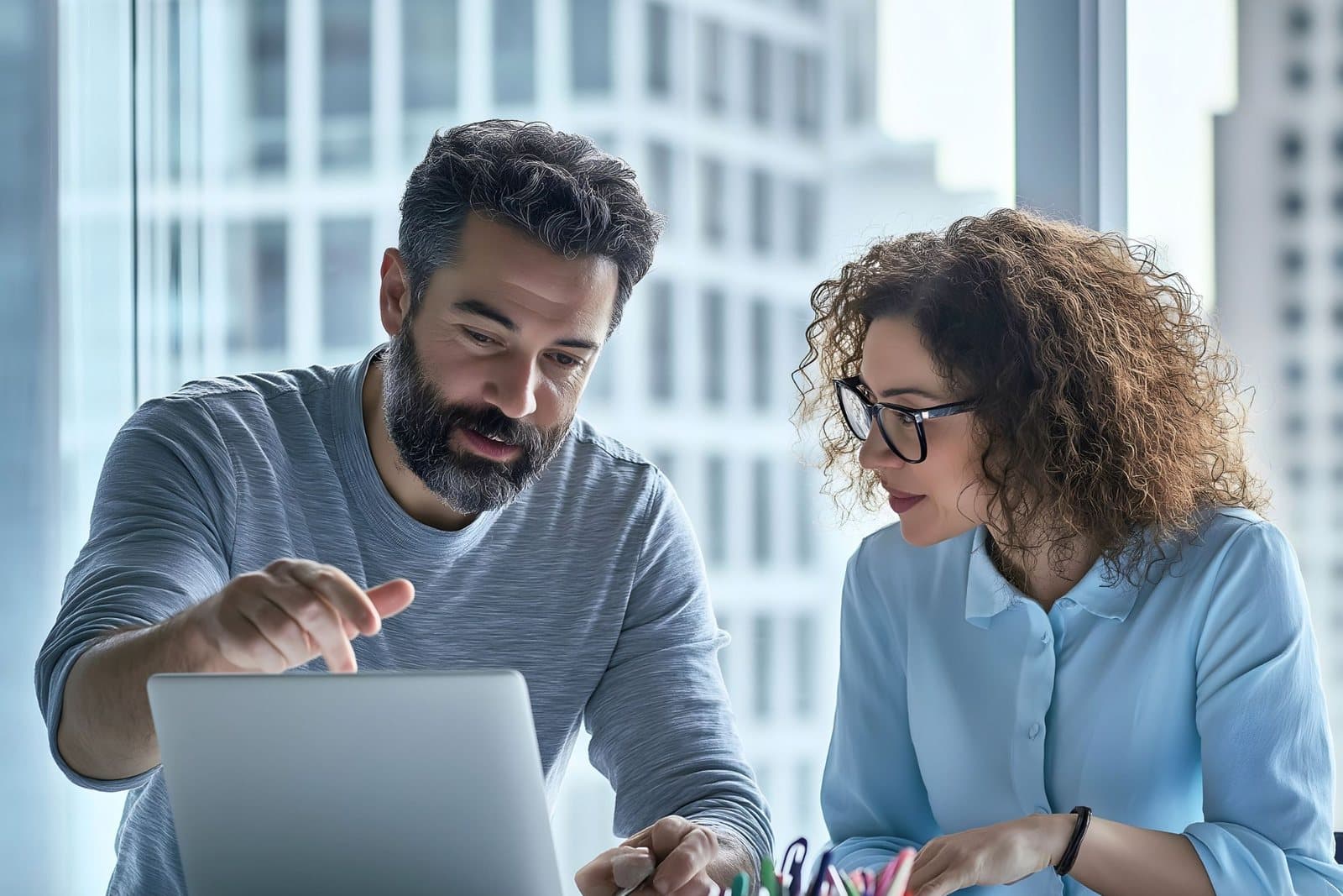 A man and a woman looking at a laptop together at a desk in a bright office