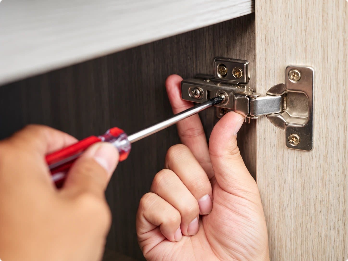Hands adjusting a cabinet door hinge with a screwdriver